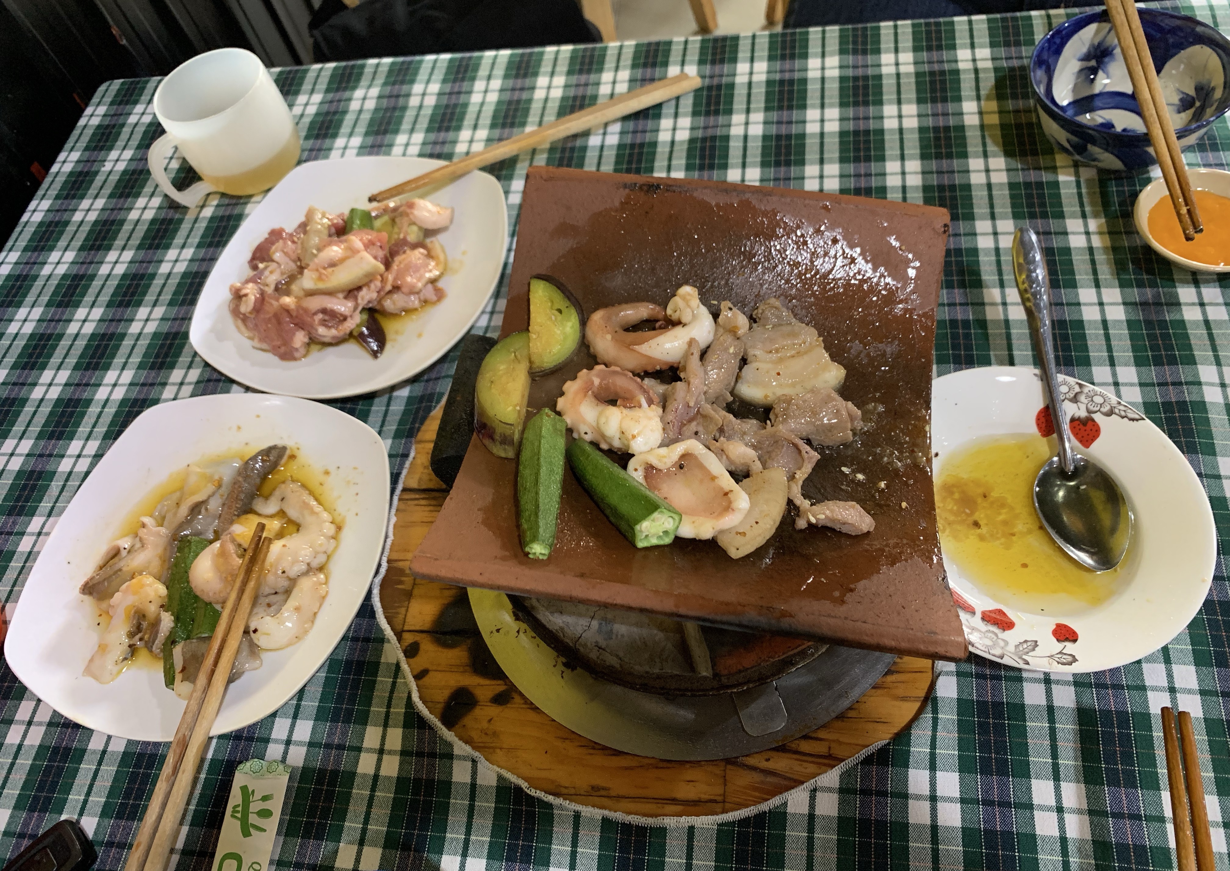 Bàn nướng ngói với hải sản, thịt ướp, rau xanh và chén nước chấm tại Quán Nướng Ngói Cu Tây