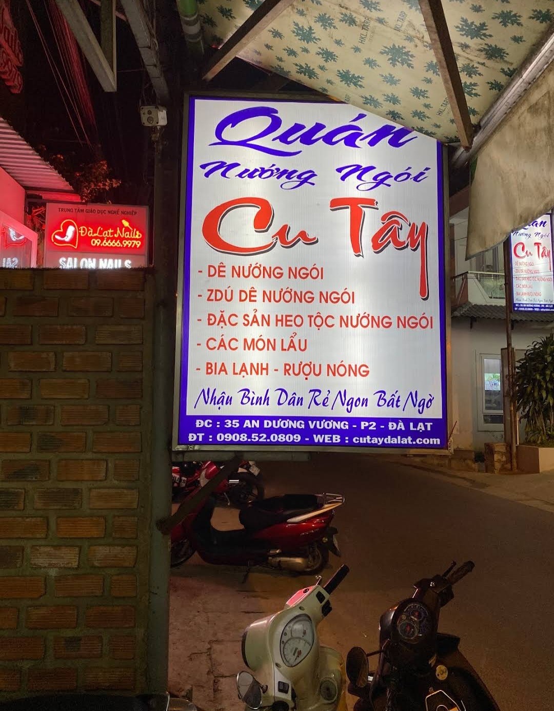Bảng hiệu đêm của Quán Nướng Ngói Cu Tây ghi dê nướng ngói, lẩu, bia lạnh và rượu nóng